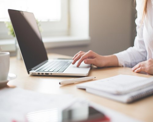 A person typing on a laptop with soft morning light coming from the window